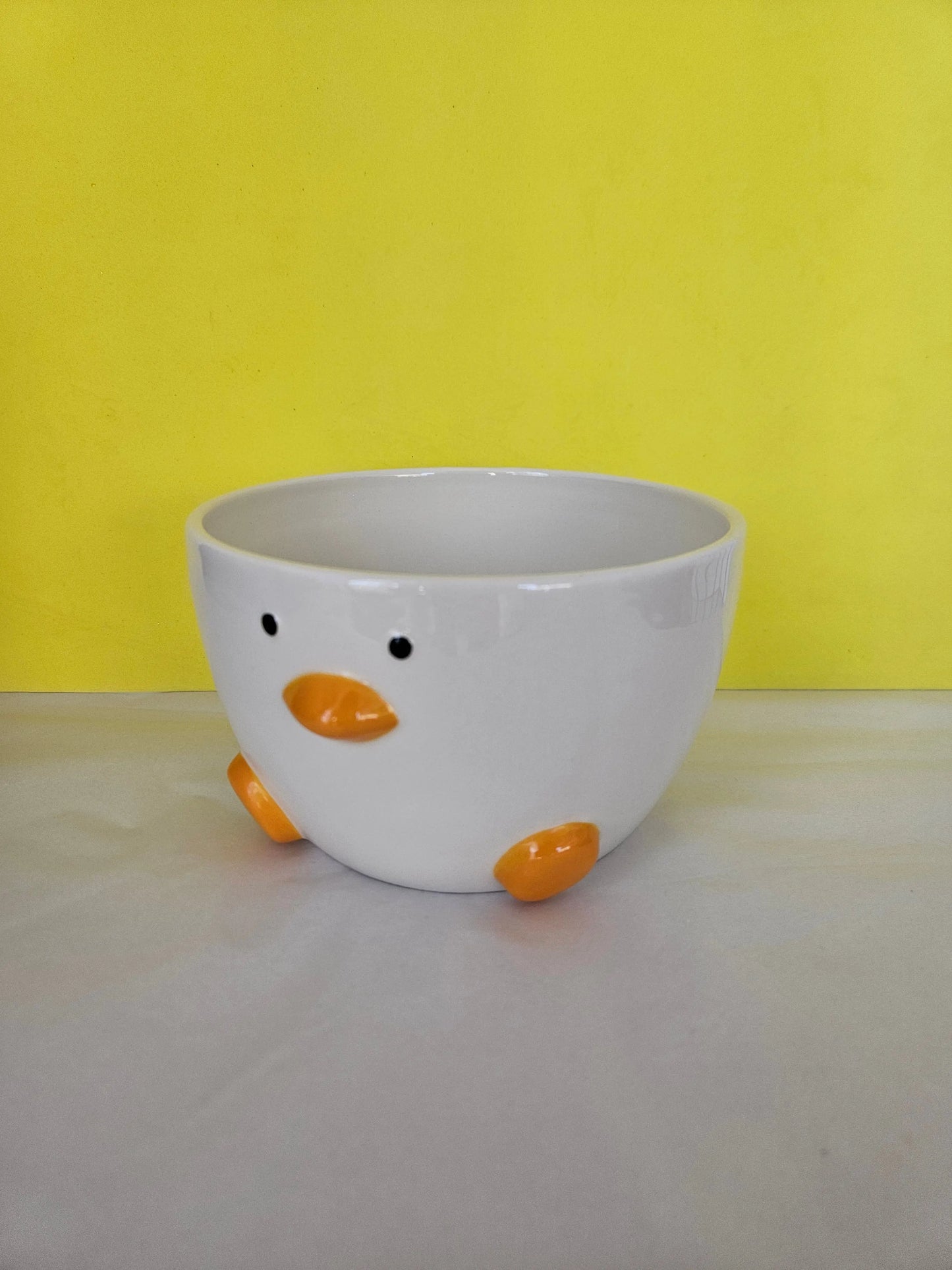 A ceramic white bowl, with orange feet and beak and two dots for eyes. The bowl is made to look like a duck.