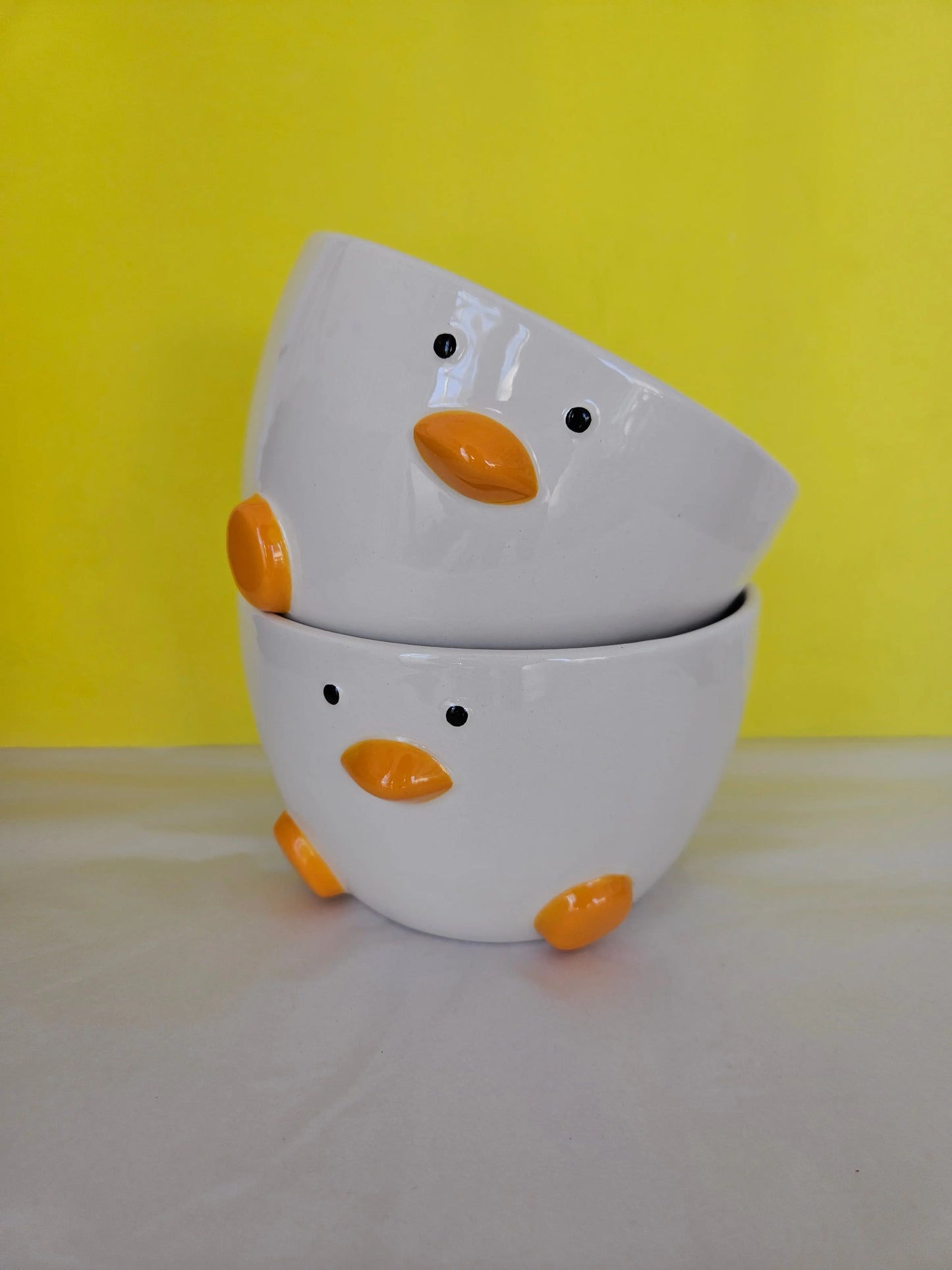 Two ceramic white bowl, with orange feet and beak and two dots for eyes. The bowl is made to look like a duck.