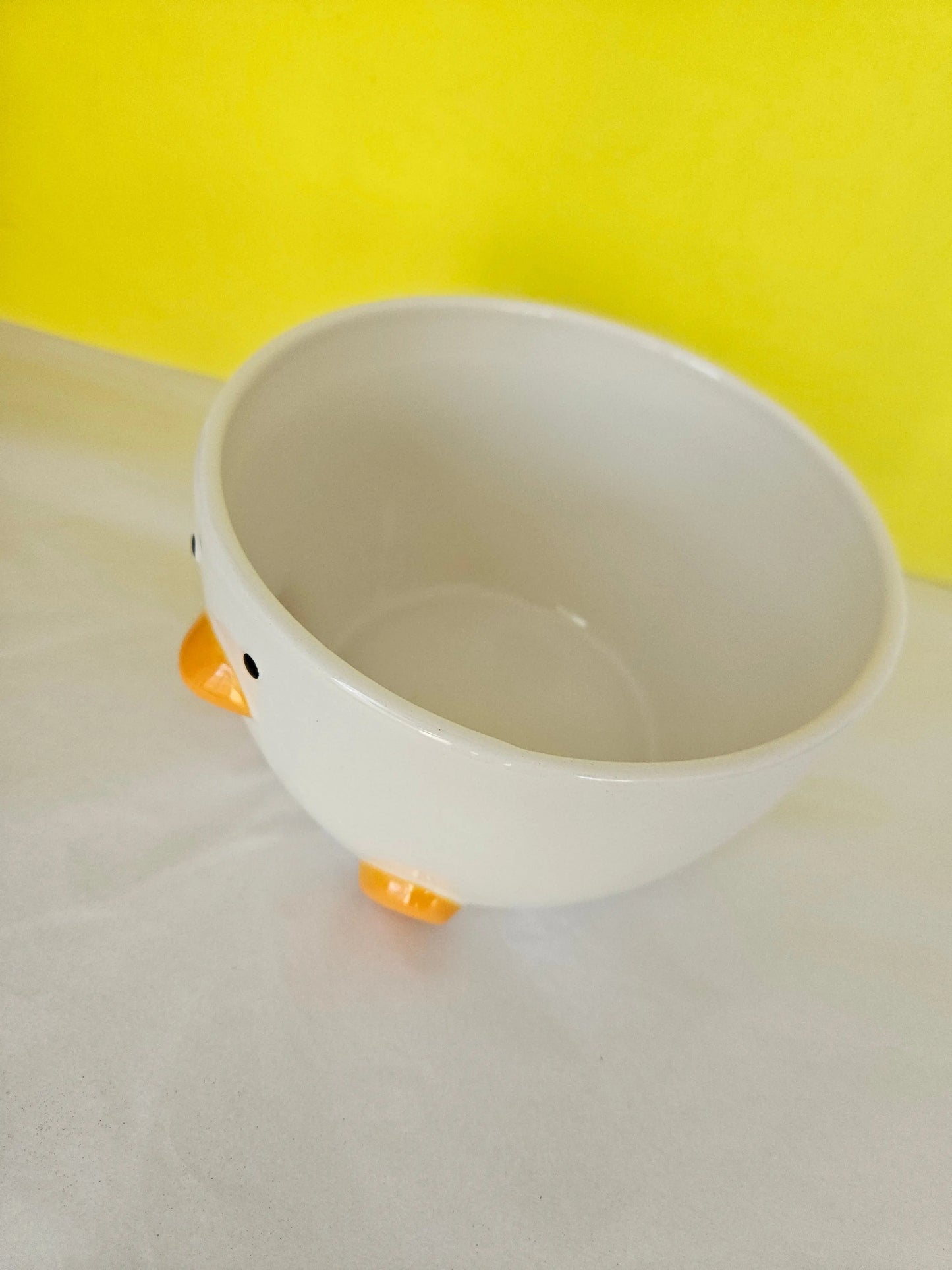 A ceramic white bowl, with orange feet and beak and two dots for eyes. The bowl is made to look like a duck.