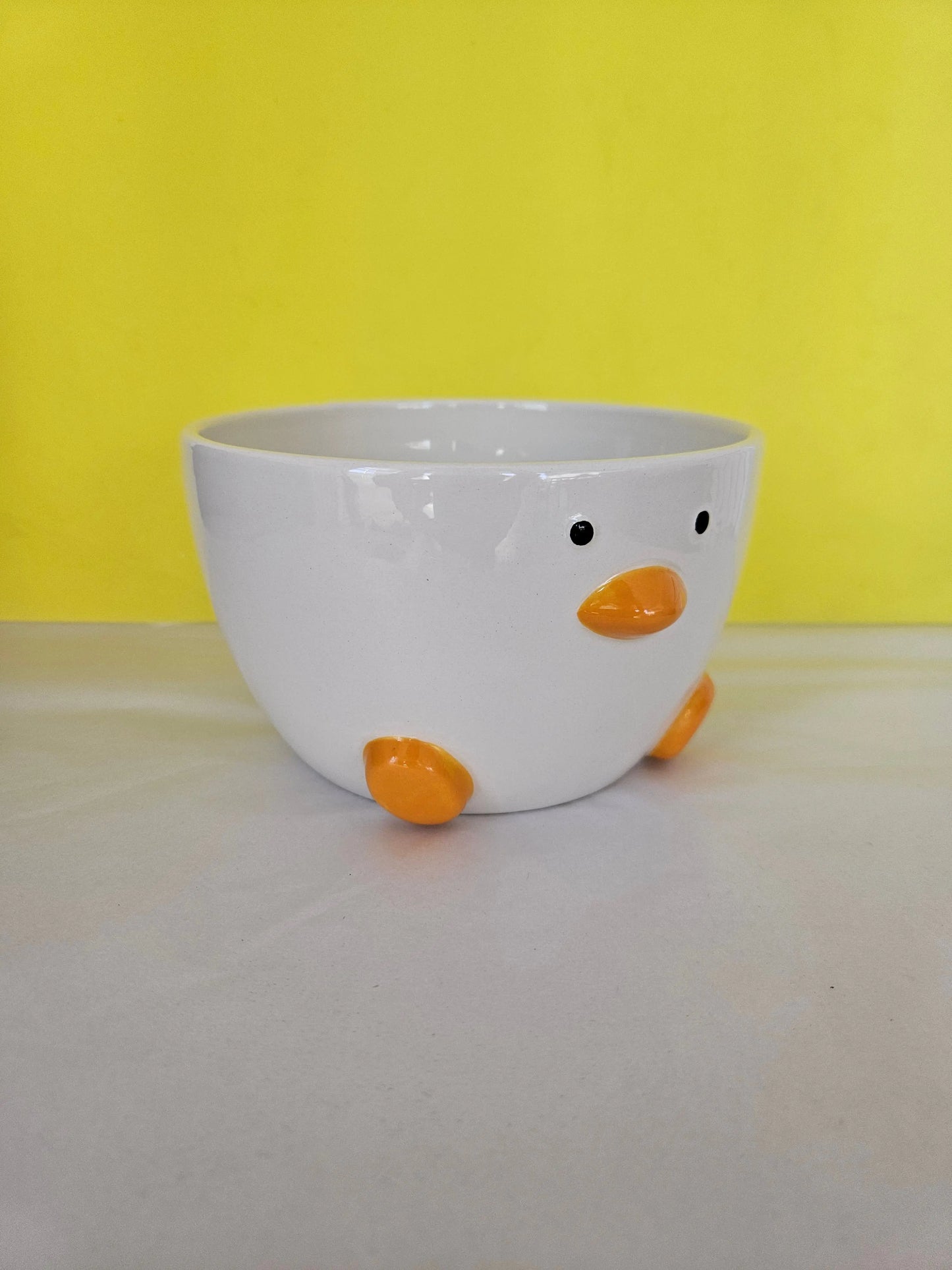 A ceramic white bowl, with orange feet and beak and two dots for eyes. The bowl is made to look like a duck.