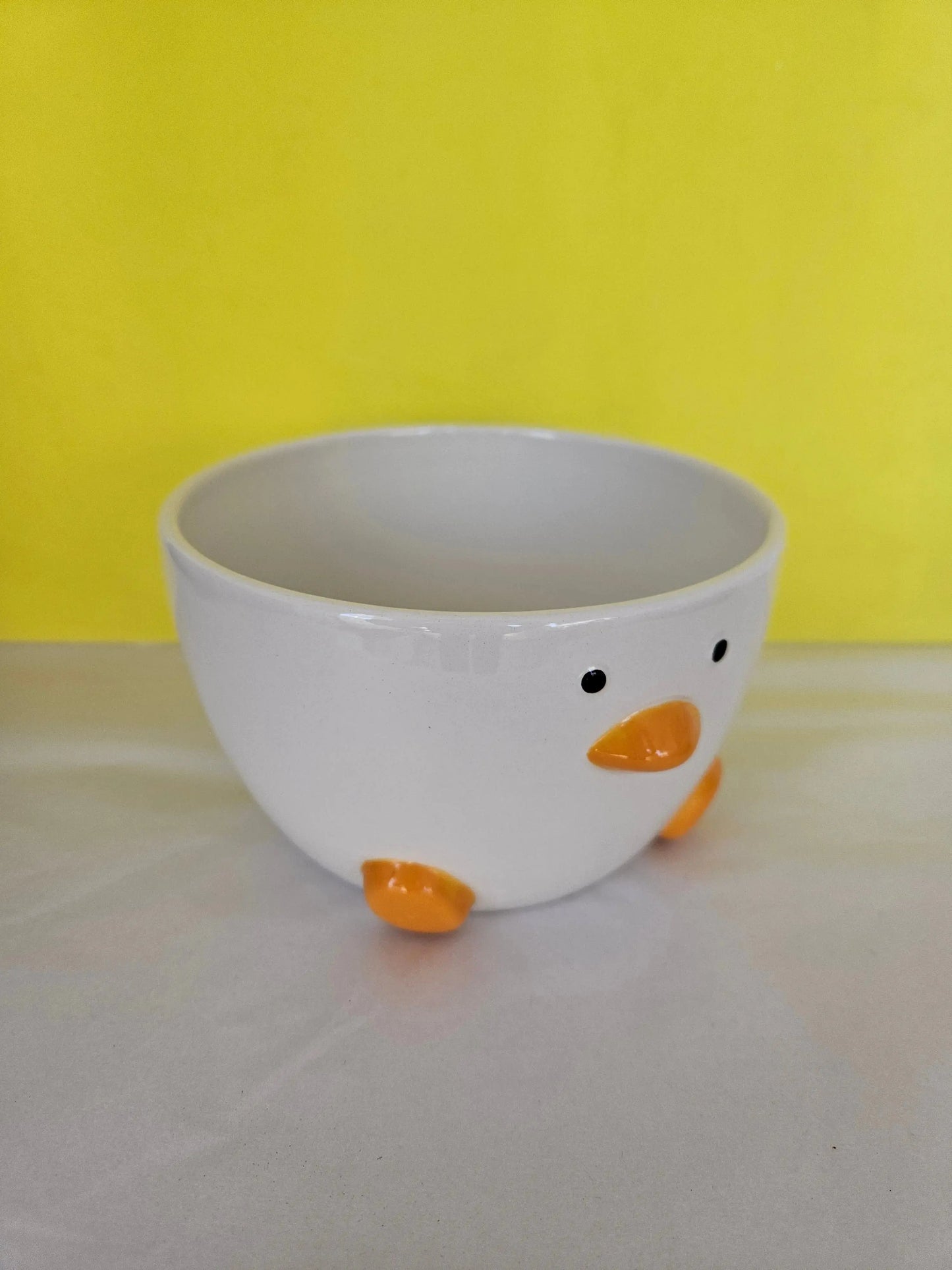 A ceramic white bowl, with orange feet and beak and two dots for eyes. The bowl is made to look like a duck.