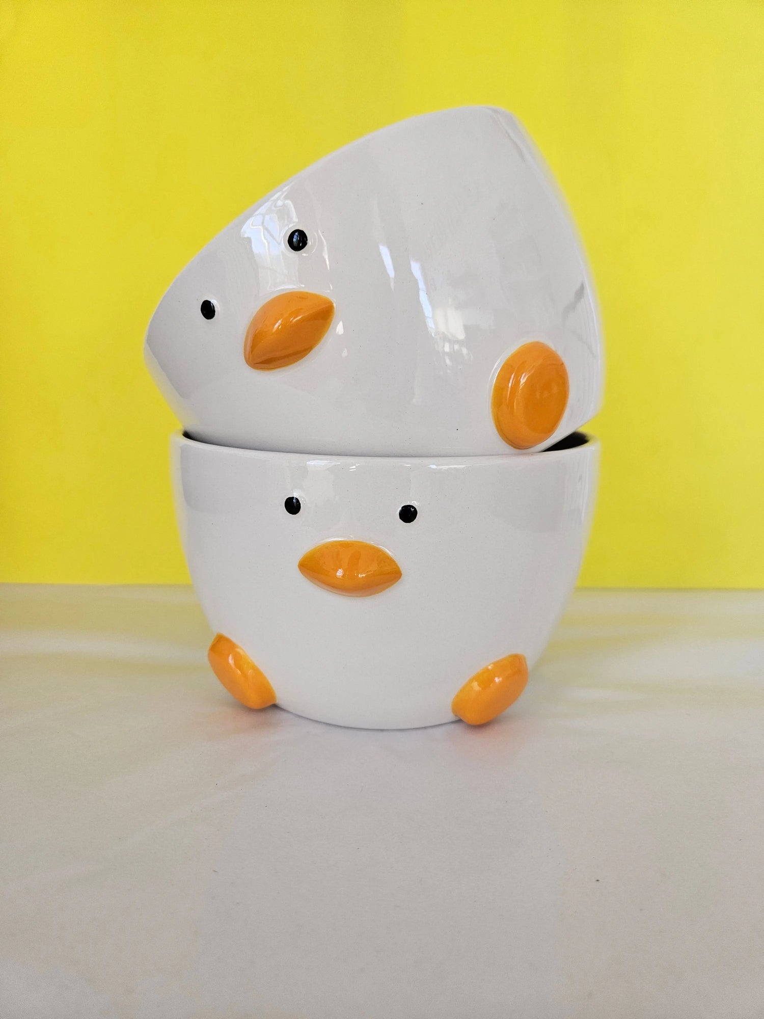Two ceramic white bowl, with orange feet and beak and two dots for eyes. The bowl is made to look like a duck.