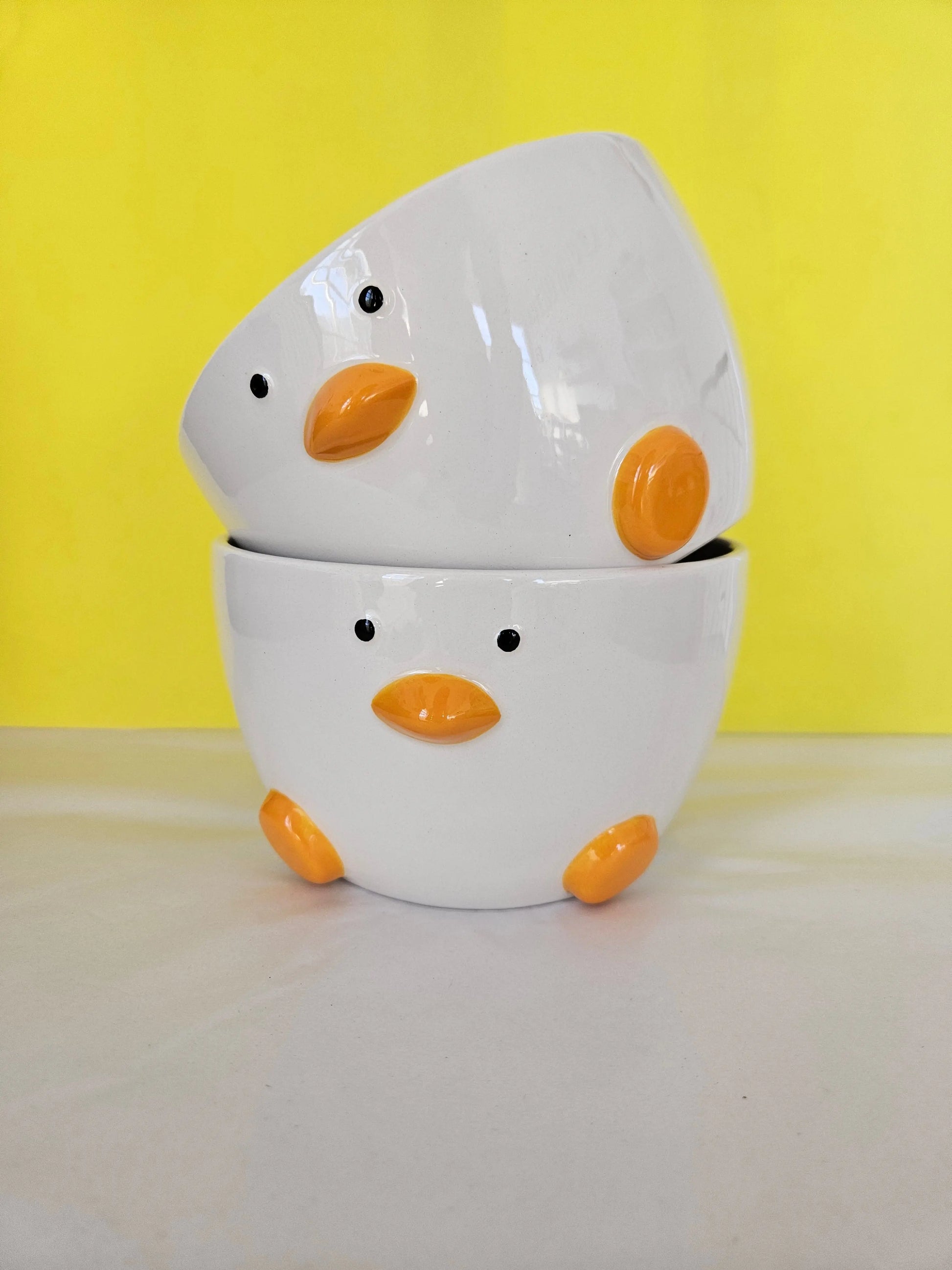 Two ceramic white bowl, with orange feet and beak and two dots for eyes. The bowl is made to look like a duck.