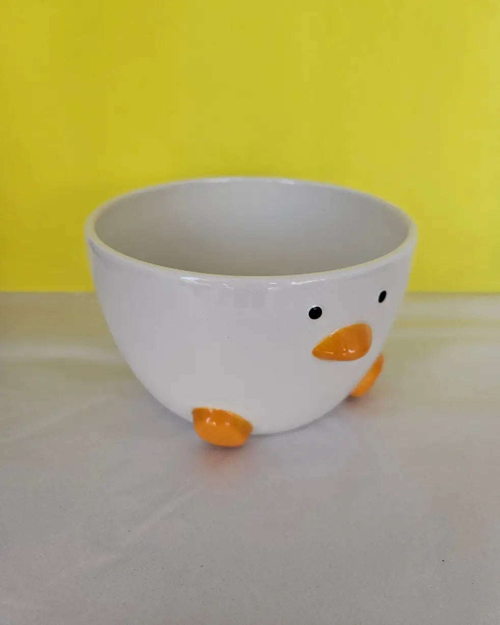 A ceramic white bowl, with orange feet and beak and two dots for eyes. The bowl is made to look like a duck.